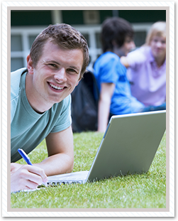 Happy high school student outside on the grass working on his laptop